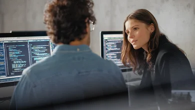 Eine Frau und ein Mann sitzen vor zwei Computern und diskutieren