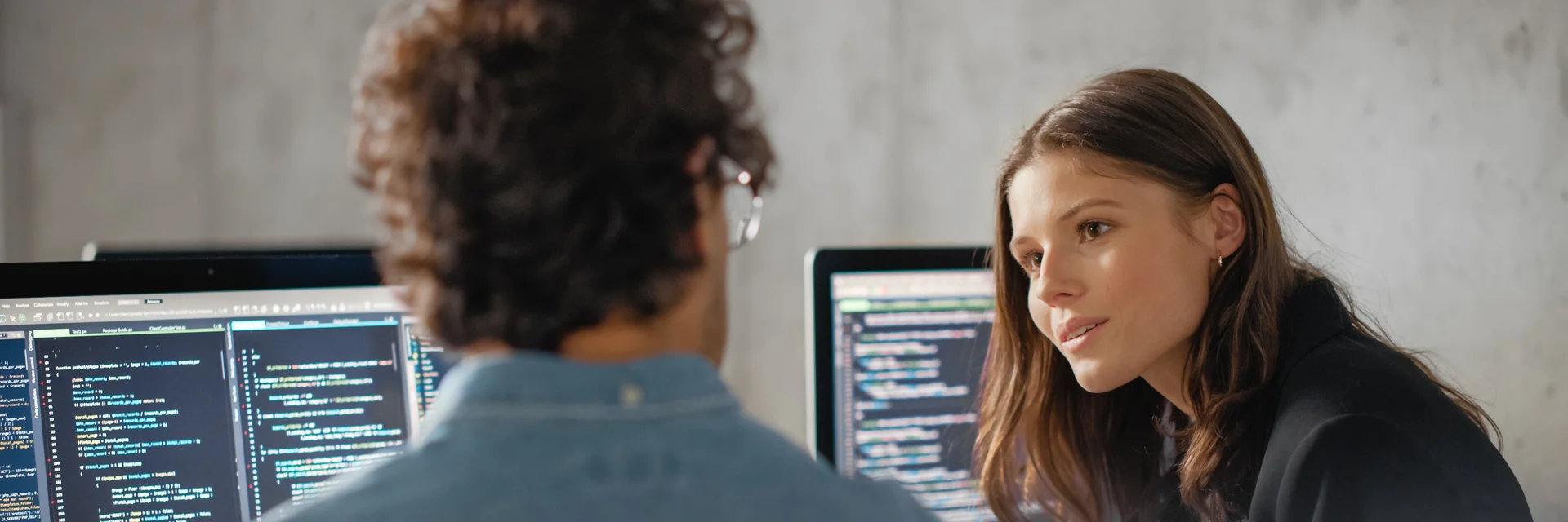 Eine Frau und ein Mann sitzen vor zwei Computern und diskutieren