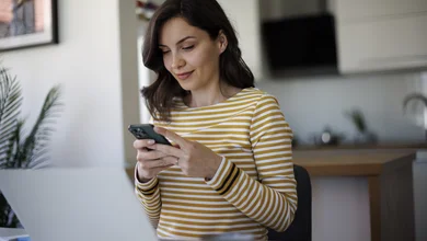 Frau in gestreiftem Shirt schaut lächelnd auf ihr Smartphone.