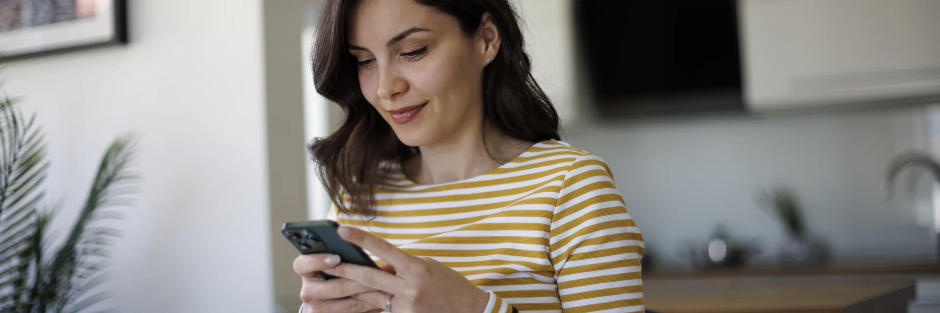 Frau in gestreiftem Shirt schaut lächelnd auf ihr Smartphone.