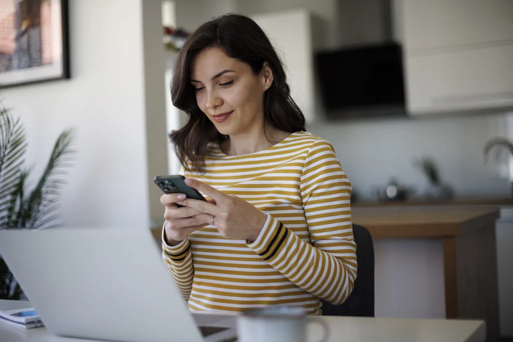 Frau in gestreiftem Shirt schaut lächelnd auf ihr Smartphone.