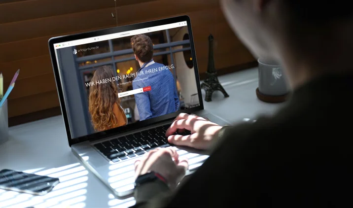 Eine Frau sitzt an einem Laptop, auf dem Bildschirm ist die Website zu sehen