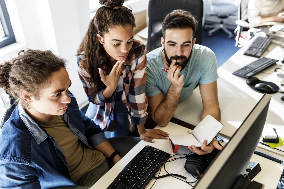 Zwei Männer und eine Frau schauen auf einen Computer.