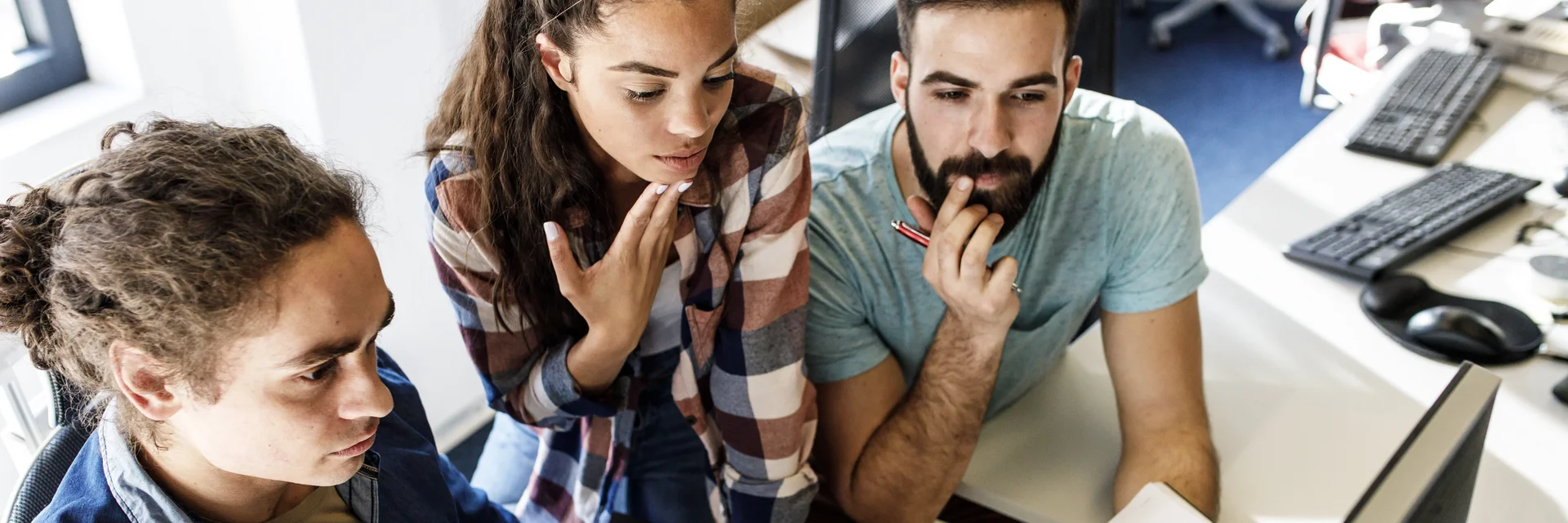 Zwei Männer und eine Frau schauen auf einen Computer.