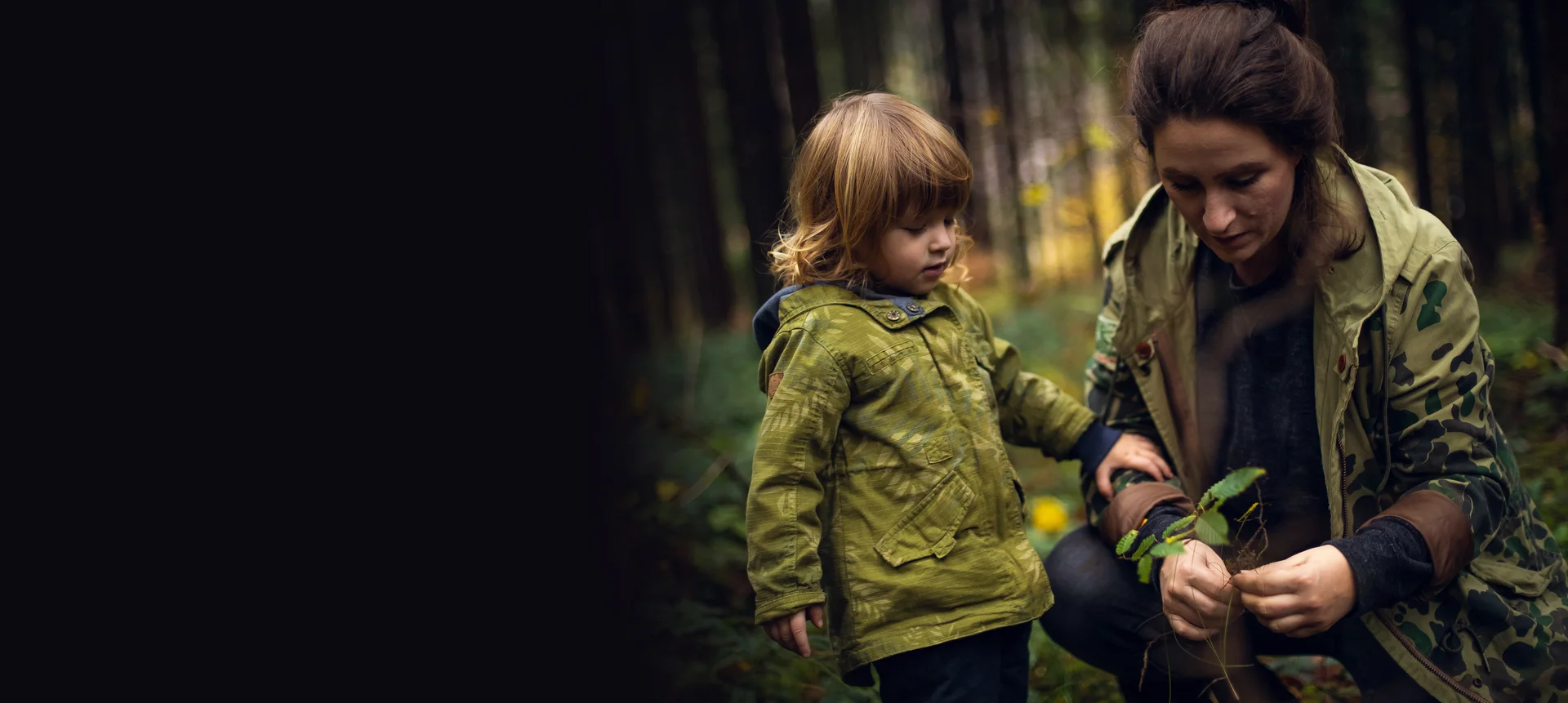 Ein Kind mit Mutter im Wald, die sich Pflanzen anschauen